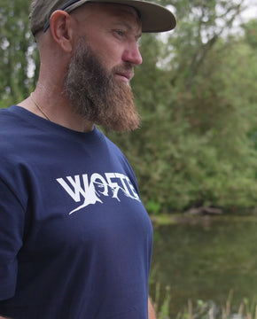 A man wearing a Wofte Peaks t-shirt with a white mountain print whist carp fishing.